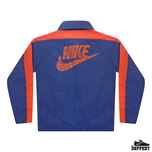 The back of a Nike windbreaker jacket in royal blue with orange shoulder yokes, sleeve stripes, and a distressed orange Nike logo and swoosh on the back.