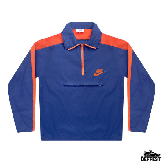 A vintage 70s Nike windbreaker pullover jacket in royal blue with bright orange shoulder panels, sleeve stripes, and zipper trim, featuring a small orange Nike swoosh on the left chest.