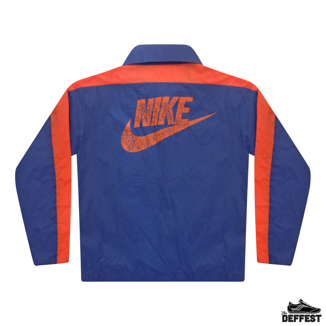 The back of a Nike windbreaker jacket in royal blue with orange shoulder yokes, sleeve stripes, and a distressed orange Nike logo and swoosh on the back.