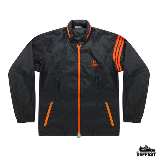 A black Adidas windbreaker jacket with bright orange accents, including the front zipper, inner collar, zippered hand pockets, and signature three stripes on the sleeves. The Adidas trefoil logo is visible on the left chest.