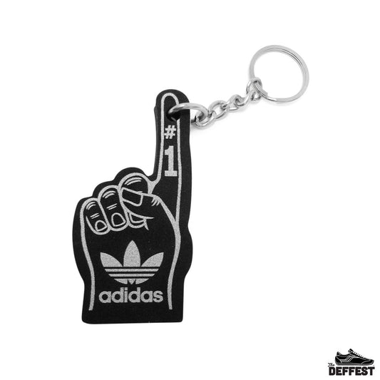 A black Adidas foam finger keychain with a silver metal chain and key ring, featuring the Adidas trefoil logo and the word 'adidas' on the palm side, and '#1' printed on the index finger.