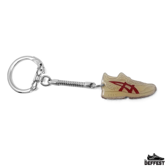 A miniature keychain shaped like a beige and red running shoe, attached to a silver metal spring ring.